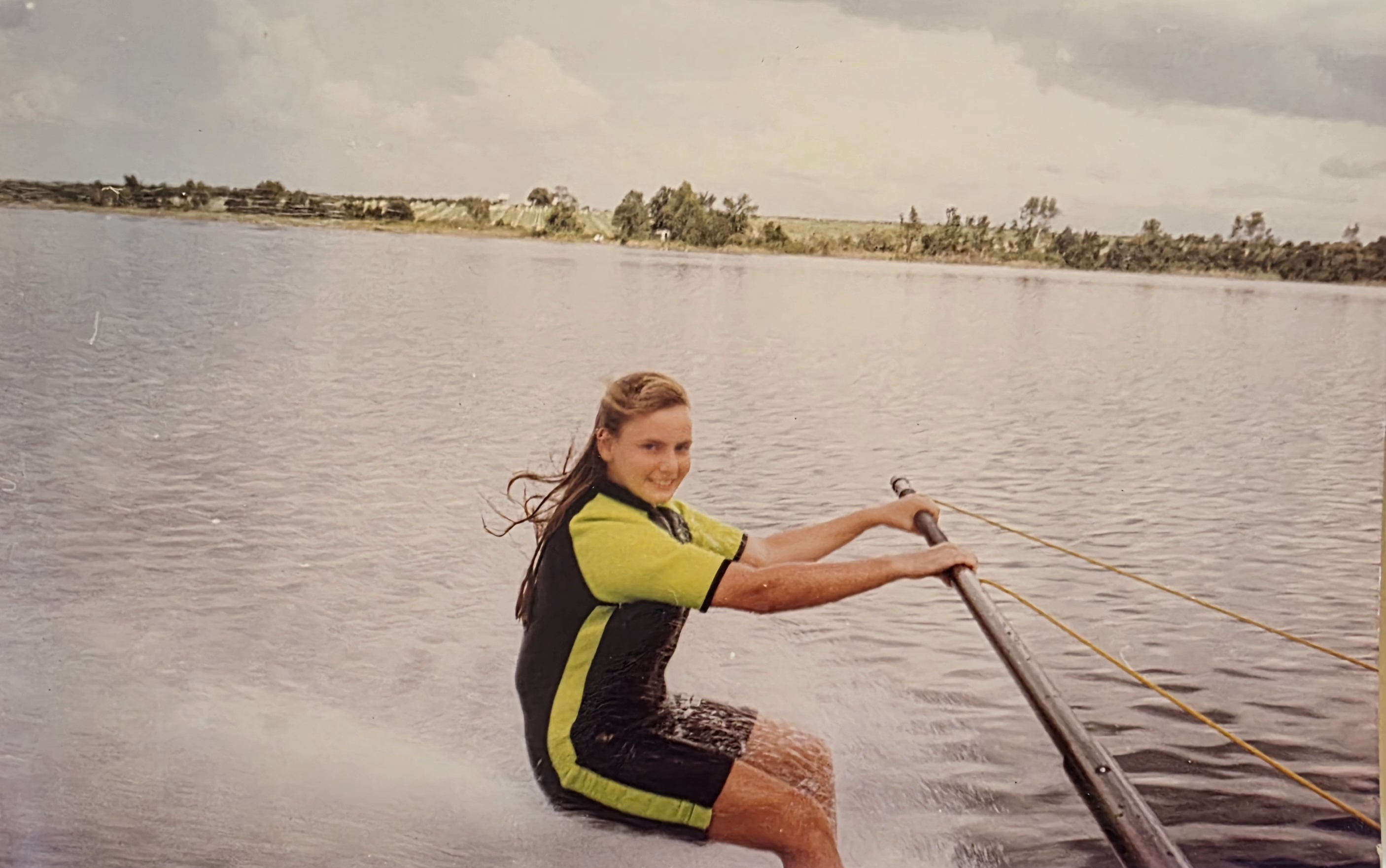 Teenage girl water skiing, barefoot, smiling for the camera.