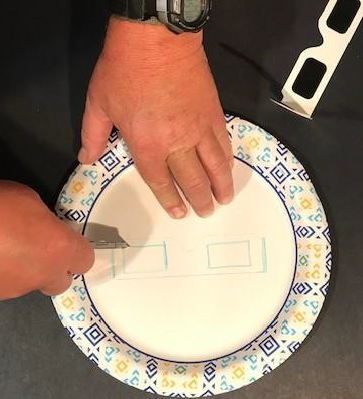 Hands cutting holes in the paper plate for the lenses.